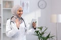 Smiling female muslim doctor with hijab using tablet to consult patients in clinic office