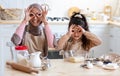 Cheerful muslim mom and her little daughter fooling together in kitchen