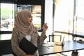 A cheerful muslim  woman in abaya standing in office hand holding document file while looking out of window. Royalty Free Stock Photo