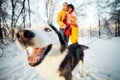 Cheerful muzzle of a dog husky in a winter park, in the background a young couple