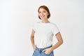 Cheerful natural girl in t-shirt and jeans smiling, looking upbeat, standing against white background