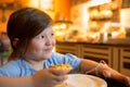 Cheerful nice little girl sitting at the table while eating sweet cake Royalty Free Stock Photo