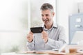 Cheerful office worker connecting with his smartphone, he is watching a video and social networking