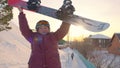 Cheerful old woman rising up hands with snowboard after successful on snow slope