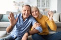 Cheerful Older Couple Waving Hands To Camera Sitting At Home Royalty Free Stock Photo