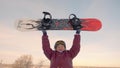 Cheerful older woman rising up snowboard on snowy slope at winter resort