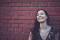 Cheerful optimistic brunette at the red brick wall, laughing with closed eyes