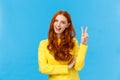 Cheerful outgoing and happy charismatic redhead female in yellow sweater, showing peace sign, number two or twice and