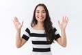 Cheerful outgoing young asian woman saying hi and smiling friendly, raising hands waiting in greeting or goodbye