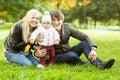 Cheerful parents with daughter sitting on grass in autumn park Royalty Free Stock Photo