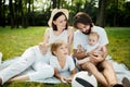 Cheerful parents with two kids dressed in white clothes is sitting on a striped blanket on the lawn on a warm sunny day Royalty Free Stock Photo