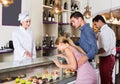 Cheerful pastry woman is offering cakes from showcase