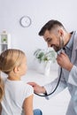 Cheerful pediatrician examining kid with stethoscope