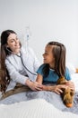 Cheerful pediatrician with stethoscope calming patient