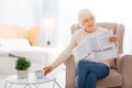 Cheerful pensioner drinking tasty tea while sitting with a newspaper and smiling