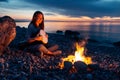 Cheerful percussionist girl playing djembe sitting on beach by the fire at sunset