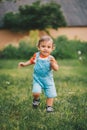 Cheerful perky toddler boy runs to meeting to camera with smile and happiness. Baby boy in denim overall in green park Royalty Free Stock Photo