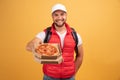 Cheerful pizza delivery man stands with carton box with pizza, waits for client, wears white cap and white tshirt with red