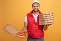 Cheerful pizza delivery man stands with carton boxes, waits for client, wears white cap and white t shirt with red waistcoat, Royalty Free Stock Photo