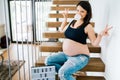 Cheerful portrait of young pregnant woman sitting on stairs enjoying life. modern lifestyle details - new home and baby coming