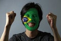 Cheerful portrait of a man with the flag of the Brazil painted on his face on grey background. The concept of sport or nationalism