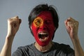 Cheerful portrait of a man with the flag of the Kyrgyzstan painted on his face on grey background.