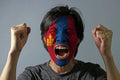 Cheerful portrait of a man with the flag of the Mongolia painted on his face on grey background.