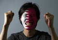 Cheerful portrait of a man with the flag of the Qatar painted on his face on grey background.