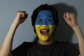 Cheerful portrait of a man with the flag of Ukraine painted on his face on grey background. The concept of sport or nationalism.