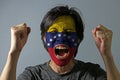 Cheerful portrait of a man with the flag of Venezuela painted on his face on grey background. The concept of sport or nationalism.