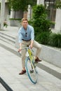 Cheerful, positive, handsome young man, employee in stylish clothes going to office by bike. Urban background
