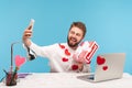 Cheerful positive man blogger with beard in white shirt covered with heart shaped stickers holding and showing on smartphone Royalty Free Stock Photo