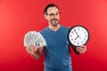 Cheerful positive man in colorful sunglasses holding money and clock while winking. Royalty Free Stock Photo