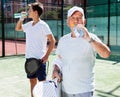 Mature man and young man drink water on padel court