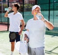 Mature man and young man drink water on padel court