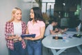 Cheerful and positive young women smile together. They stand in white room. Models hold trye and plastic tablet. Two Royalty Free Stock Photo