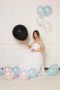 A cheerful pregnant young woman in anticipation of a baby in a white dress, isolated white neoclassical wall.