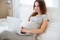 Cheerful pregnant young woman lying and using laptop on bed Royalty Free Stock Photo