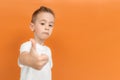 Cheerful preschooler boy in white T-shirt dress posing showing thumbs up isolated on yellow background. The child