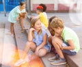 Cheerful preteen girls and boys sitting on steps outdoors and chatting