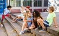 Cheerful preteen girls and boys sitting on steps outdoors and chatting