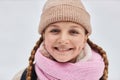 Cheerful pretty girl in warm woolen winter cap and scarf looking at camera