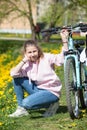 Cheerful pretty girl wearing pink hoody sitting on pathway with her blue bicycle Royalty Free Stock Photo