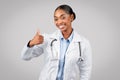 Cheerful pretty millennial black lady doctor in white coat make thumb up sign with hand Royalty Free Stock Photo
