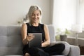 Cheerful pretty senior woman holding tablet computer, sitting on couch Royalty Free Stock Photo