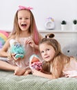 Cheerful pretty small girls sisters kids with long hair relaxing on bed and playing with toys dolls together