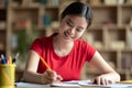 Cheerful pretty smart young chinese girl student making notes, homework, studying in living room Royalty Free Stock Photo