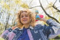 Cheerful pretty teenage woman in a blue jacket standing and holding a colorful short skateboard behind her head. Outdoor Royalty Free Stock Photo