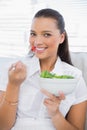 Cheerful pretty woman eating healthy salad sitting on sofa Royalty Free Stock Photo