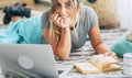 Cheerful pretty young adult woman smile and enjoy time reading a book at home lay down on the floor - open laptop computer to use Royalty Free Stock Photo